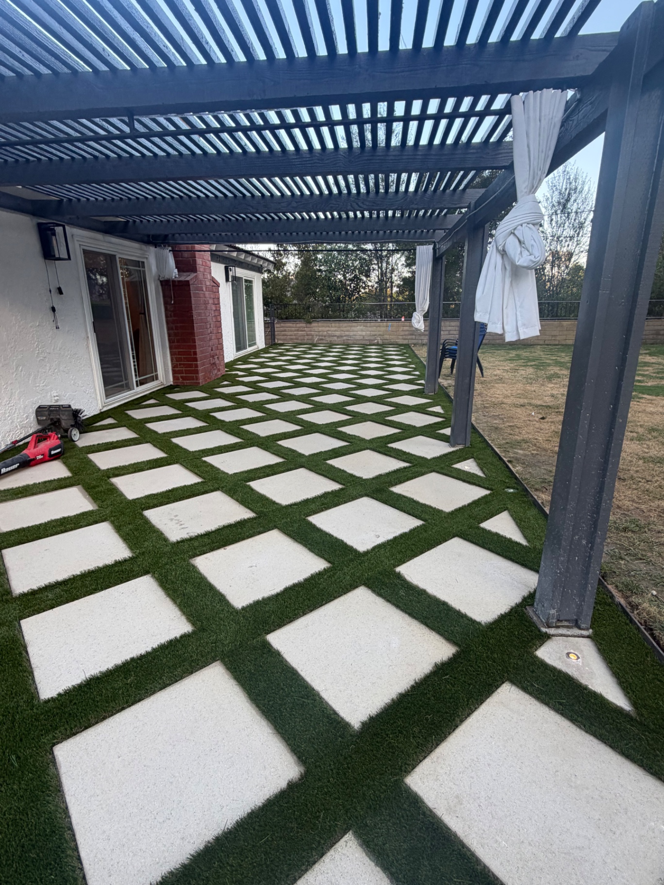 Backyard pergola over a checkerboard paver and turf patio