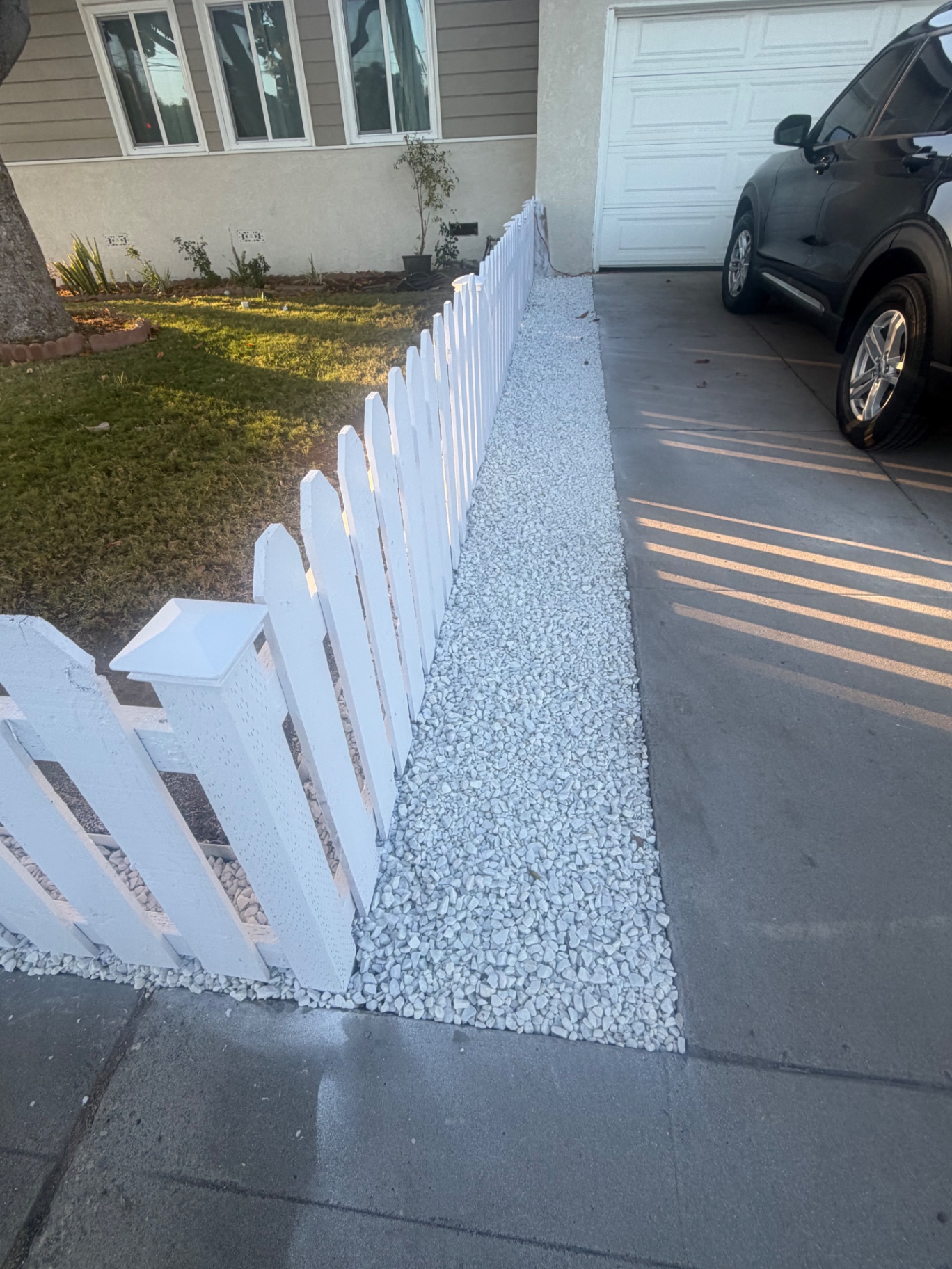 White picket fence with a clean white gravel border by the driveway